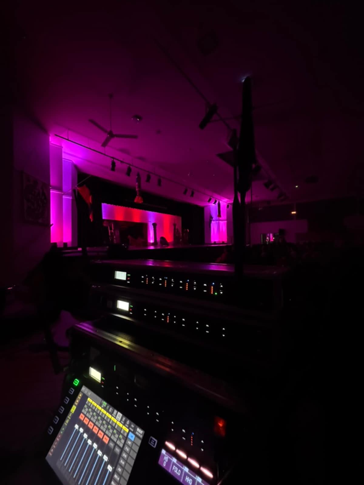 Two Shure ULXD wireless receivers stacked at FOH during a theatre production with 14 active headset channels, with the lit stage visible in the background under purple stage wash